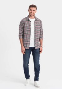 Camicia a quadri in rosso, bianco e blu marina con maniche arrotolate, indossata sopra una maglietta bianca semplice. Abbinata a jeans scuri e scarpe bianche.