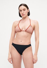Triangle bikini top in orange geometric print with thin straps; paired with black high-waisted bikini bottoms featuring cutout accents.