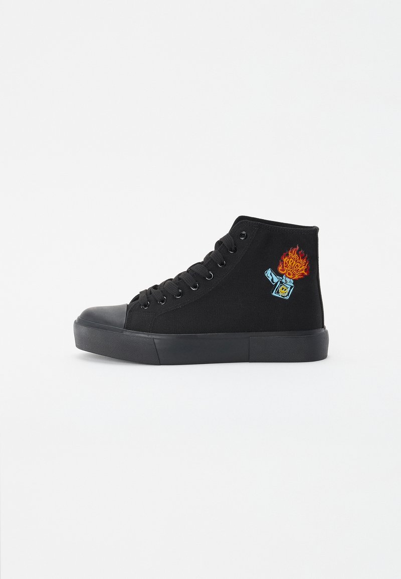 Baskets montantes noires avec semelle et lacets noirs, ornées d'un patch représentant un briquet bleu avec une flamme rouge et orange sur le côté.