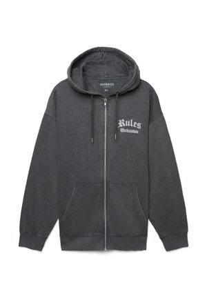 Felpa con cerniera oversize di colore grigio scuro, dotata di tasche frontali, cappuccio con coulisse e testo bianco "Regole Sconosciute" sul lato sinistro del petto.