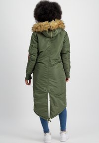 Olivno zeleni dolgi puffer plašč s umetnim krznom na kapuci, rebrastimi manšetami in asimetričnim robom. Ima stranske žepe in zadrgo za zapiranje.