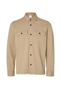 Beige långärmad skjorta med knappfront, två bröstfickor, svarta tryckknappar och spetsig krage, visad mot en vit bakgrund.