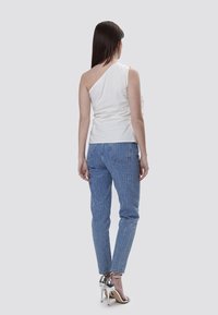 Hvid én-skulder top parret med stribede blå denim jeans. Jeansene har en slim fit med vertikale hvide striber og har en subtil tekstur.