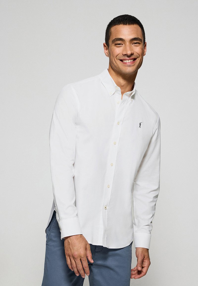 Wit overhemd met lange mouwen en knopen, voorzien van een klein logo op de borst, gecombineerd met lichtblauwe broek. Gladde stof met een klassieke kraag.