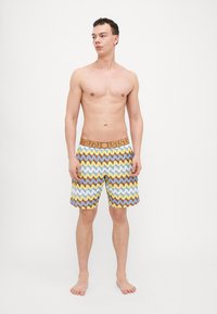 Färggranna badshorts med ett zigzagmönster i gult, blått och brunt, med en enfärgad brun midja prydd med en logotyp.