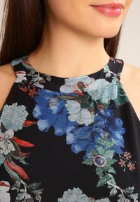 Haut noir sans manches avec un motif floral comprenant des fleurs bleues, blanches et rouges ; tissu lisse avec un léger éclat ; encolure ronde.