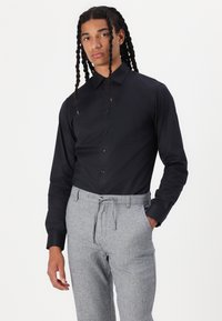 Black button-up shirt with a pointed collar, paired with light grey, drawstring trousers featuring a textured pattern.