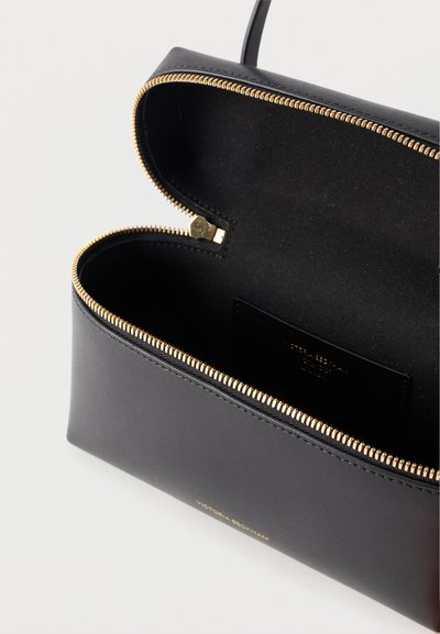 Μαύρο δερμάτινο τσαντάκι χειρός με ανοιχτό χρυσό φερμουάρ και εσωτερική τσέπη, που δείχνει το λογότυπο «Victoria Beckham» ανάγλυφο σε χρυσό στο μπροστινό μέρος.