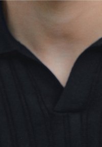 Lähikuva ihmisen kaulasta ja ylärinnasta, joka on pukeutunut mustaan kauluspaitaan, jossa on hienovaraisia pystysuoria raitoja.
