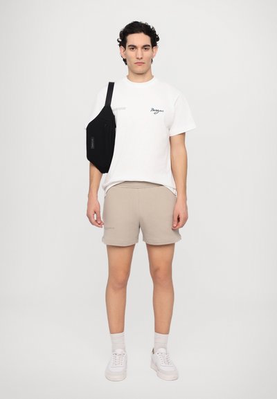 Bolso de mensajero negro, camiseta de manga corta blanca con gráfico, pantalones cortos beige, zapatillas blancas, corte relajado, textura suave, colores neutros.
