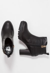 Et par sorte læderstøvler til anklerne med blokhæl, sidezipper og dekorative spænder på en hvid baggrund.