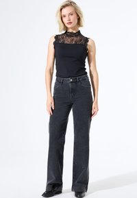 Top negro sin mangas con encaje y bordes con volantes, combinado con unos vaqueros negros de cintura alta, ligeramente desgastados. Textura lisa, ajuste casual.
