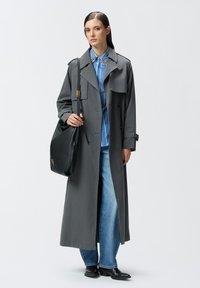 Cappotto grigio con design doppiopetto, abbinato a una camicia a righe blu, jeans a campana e stivaletti neri in pelle. Borsa nera.