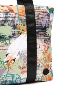 Tote bag met een levendige, graffiti-achtige print, voorzien van een witte, textuur oppervlakte, zwarte riemen en een ronde logo patch.