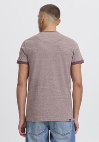 Camiseta marrón de brezo con cuello redondo y mangas cortas, que presenta un ribete de color burdeos en los bordes de las mangas. Tejido texturizado.