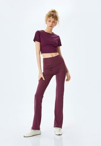 Bordeaux crop top en flared leggings gemaakt van zachte, elastische stof; minimalistisch ontwerp met een getailleerde silhoutte en subtiele accenten.