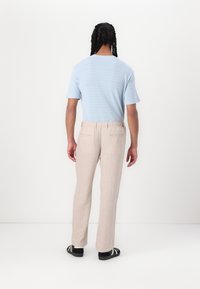 Lyseblå strikket kortermet topp kombinert med beige linbukser med snor i livet og to baklommer. Svarte sandaler fullfører antrekket.
