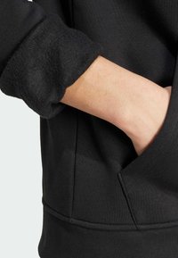 Černá fleecová mikina s texturovaným manžetami, viditelnými švy a přední kapsou. Hladká látka s těsným střihem.