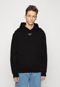 Felpa nera in misto cotone, con tasca a marsupio frontale, coulisse regolabili e logo "Calvin Klein Jeans" bianco.
