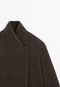 Tmavě hnědý vlněný kabát s vysokým límcem zapínaným jedním černým knoflíkem na levé straně.