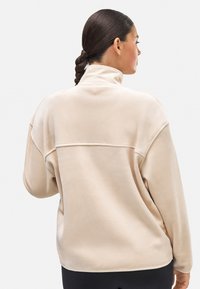 Sudadera de forro polar beige con cuello alto, corte relajado y detalle de costura en contraste en la espalda. Textura suave, sin logotipos visibles.