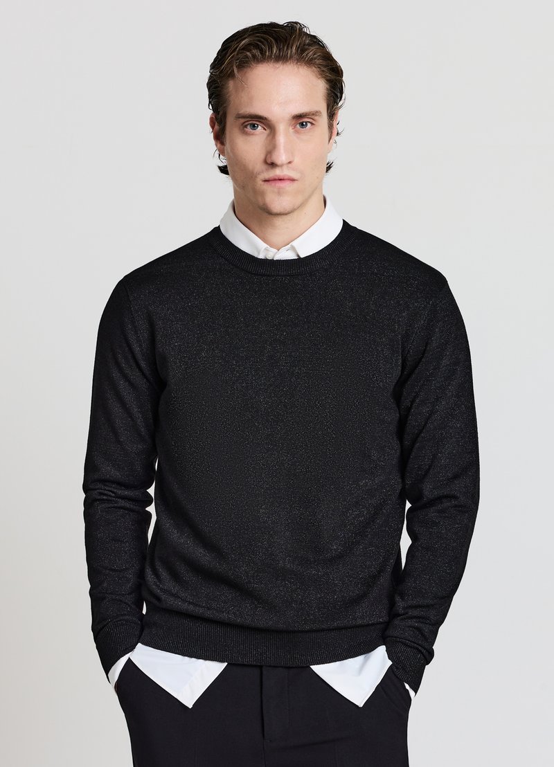 Pull noir en maille avec col rond, manches longues et motif texturé. Porté sur une chemise blanche à col, avec des poignets et un ourlet côtelés.