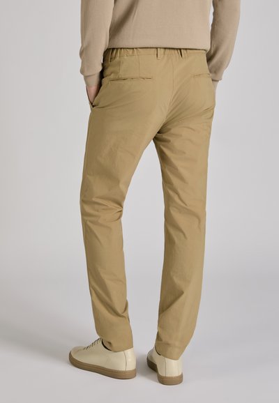 Beige, lightweight trousers with an elastic waistband, featuring two back pockets and a tapered design, paired with light-colored shoes.