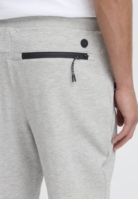 Gray sweatpants featuring a black zippered pocket at the back, with a textured, soft fabric and adjustable drawstring detail.