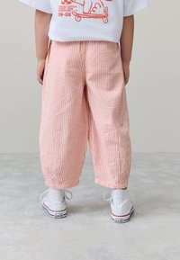 Pantaloni larghi a righe rosa e bianche con finitura testurizzata, indossati con sneakers alte bianche, visti da dietro.
