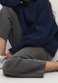 Granatowy sweter z dzianiny o teksturowym wykończeniu i opuszczonymi ramionami, zestawiony z szarymi spodniami o szerokich nogawkach i białymi sneakersami.