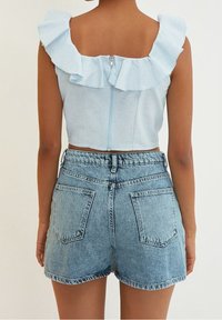 Top corto azul claro con hombros con volantes y cremallera en la espalda, combinado con pantalones cortos de mezclilla de talle alto con dobladillo deshecho y bolsillos traseros.