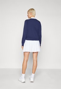 Suéter azul marino con forma ajustada y dobladillo acanalado, combinado con una falda blanca plisada, usado con zapatillas blancas y calcetines hasta el tobillo.