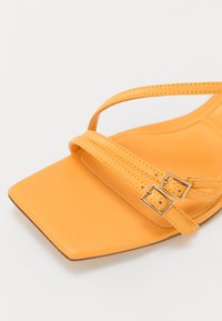 Sandale en cuir jaune avec un bout carré, dotée de deux fines sangles et d'accents à double boucle. La semelle intérieure a une texture lisse.