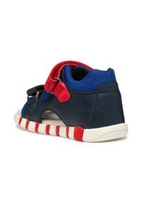 Scarpa in pelle blu e nera con accenti rossi, tomaia in rete e suola a righe bianche. Presenta una fascia regolabile per una vestibilità perfetta e fori di ventilazione.