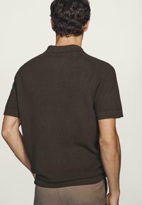 Polo marrone a maniche corte con un design a maglia strutturata e un orlo dritto. Presenta un colletto classico e linee pulite.