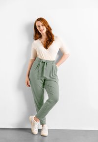 Top ribbed beige chiaro con scollatura a V e maniche corte abbinato a pantaloni a vita alta verde salvia con cintura annodata davanti e tasche.