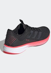 Scarpa sportiva nera con tomaia testurizzata, tre strisce grigie e suola rosa e bianca. Presenta un dettaglio posteriore perforato e un colletto imbottito.