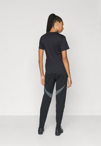 Tricou negru cu mâneci scurte, asortat cu pantaloni sport negri cu accente diagonale gri; material neted și croială ajustată.