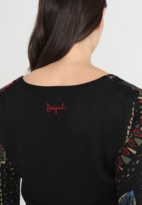 Pull noir avec manches longues à motifs. Présente un logo brodé en rouge dans le dos. Le tissu semble doux avec une finition texturée.
