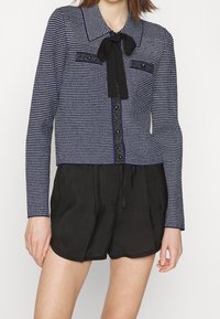 Navy ja valge mustriga kardigan krae, esipaneelil nööbid, must siidiriie, pikkade varrukatega, sobitatuna mustade lühikeste pükstega.