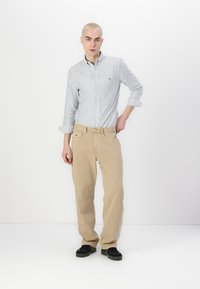 Lichtblauw en wit gestreept button-up shirt, beige katoenen broek en zwarte schoenen. Opvallende kenmerken zijn opgerolde mouwen en subtiele branding.