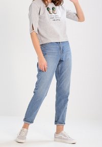 Sudadera gris corta con bordado de piña, ajuste relajado y aberturas laterales. Combinada con jeans de tiro alto azul claro y zapatillas gris.