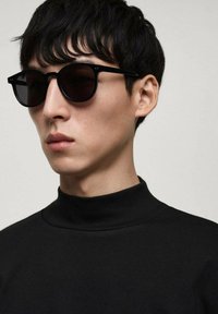 Ochelari de soare negri cu lentile rotunde, rame elegante și detalii minime. Purtați cu un top negru cu guler înalt și mâneci lungi. Textură netedă.