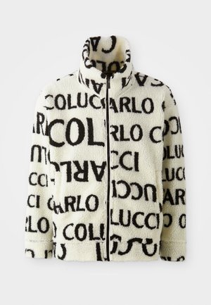 Veste en polaire crème, avec de grands motifs en texte noir. Col montant et fermeture zippée, avec poches latérales et tissu texturé.