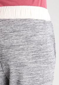 Grå joggerbyxor med en strukturerad tyg, med vit elastisk midja och sidofickor. Designen är avslappnad och funktionell.