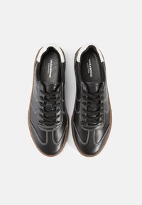 Mustad mustad nahast sneakers, millel on valged aksendid ja õmblused, ümmargune nina, tekstuuriga pind ja pruun kummist talla. Paeltega disain.