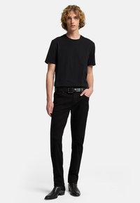 Czarny t-shirt z okrągłym dekoltem zestawiony z czarnymi dżinsami i czarnymi skórzanymi butami. Strój cechuje się minimalistycznym designem z prostym paskiem.