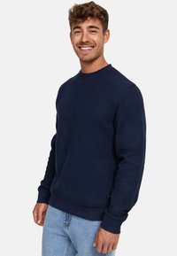 Sudadera de cuello redondo color azul marino hecha de material texturizado; cuenta con puños y dobladillo acanalados, con una pequeña etiqueta de logo en la parte inferior.