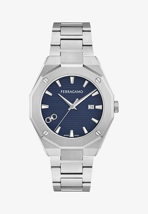 Reloj de acero inoxidable plateado con una caja octagonal, esfera texturizada de color azul marino, marcadores de hora plateados, pantalla de fecha y pulsera de eslabones. La marca "FERRAGAMO" es visible.