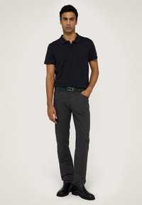 Námorně modré polo tričko s límcem s zelenými akcenty, kombinované se šedými kalhotami a odpovídajícím zeleným opaskem. Černé kotníkové boty dokončují celý outfit.